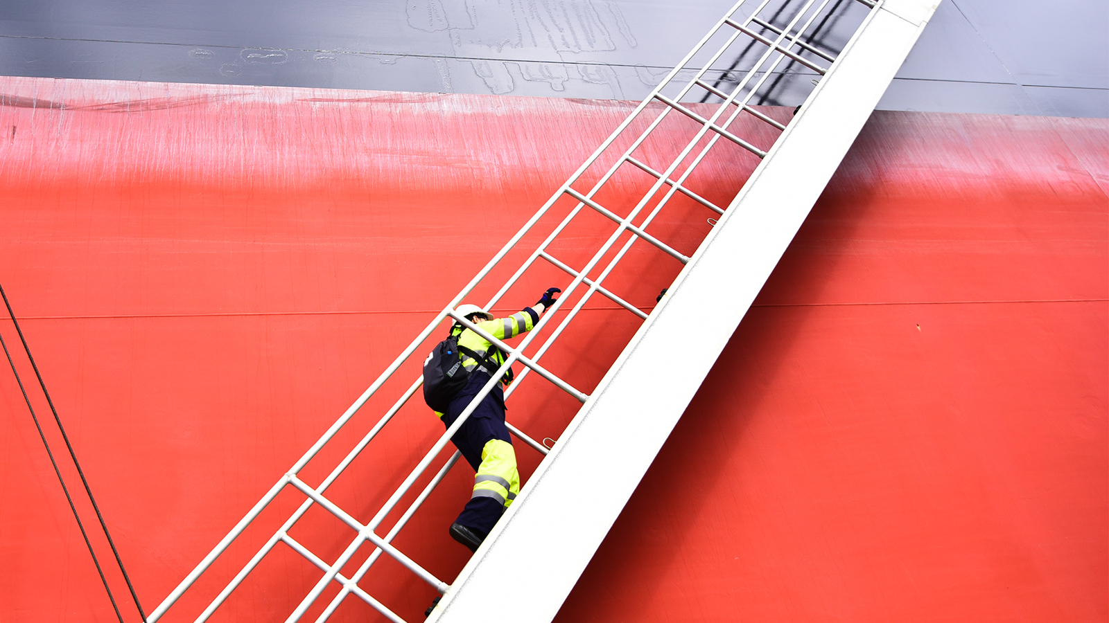 Man climbing a ladder up the hull of a vessel