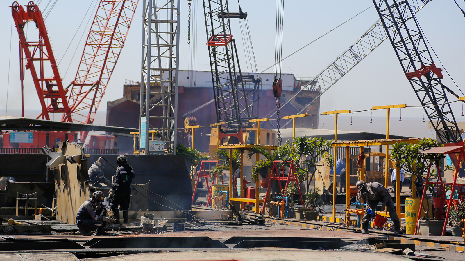 A recycling yard for ships in India, with workers in the foreground and a dismantled ship