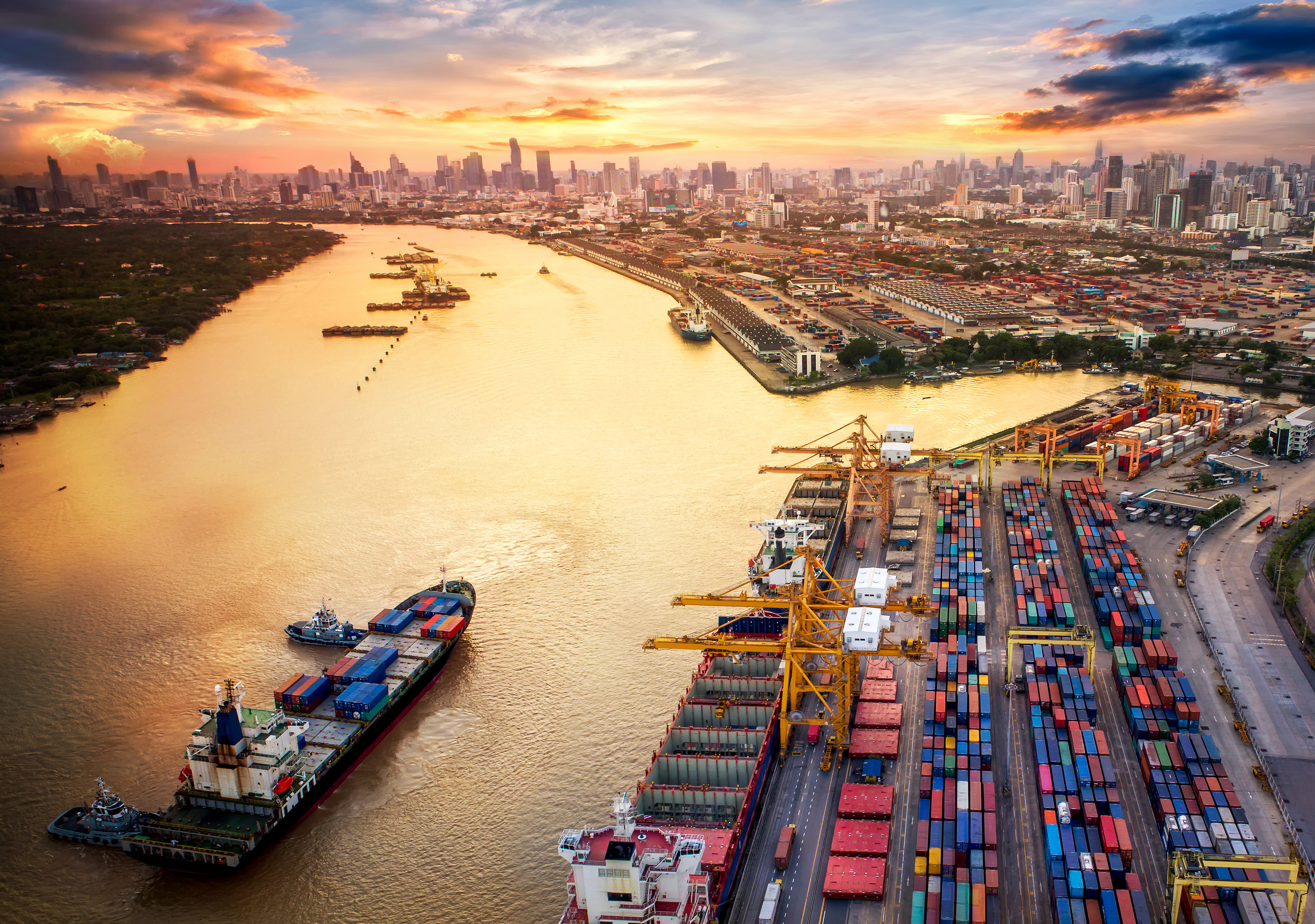 Container ship approaching a port in a river with a city skyline in the distance